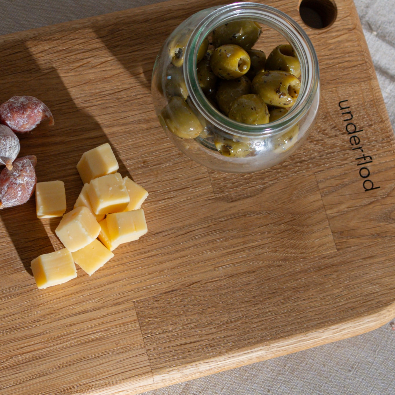 Billede taget oppe fra tapasbræt med ost, små tapaspølser og et glas med grønne oliven