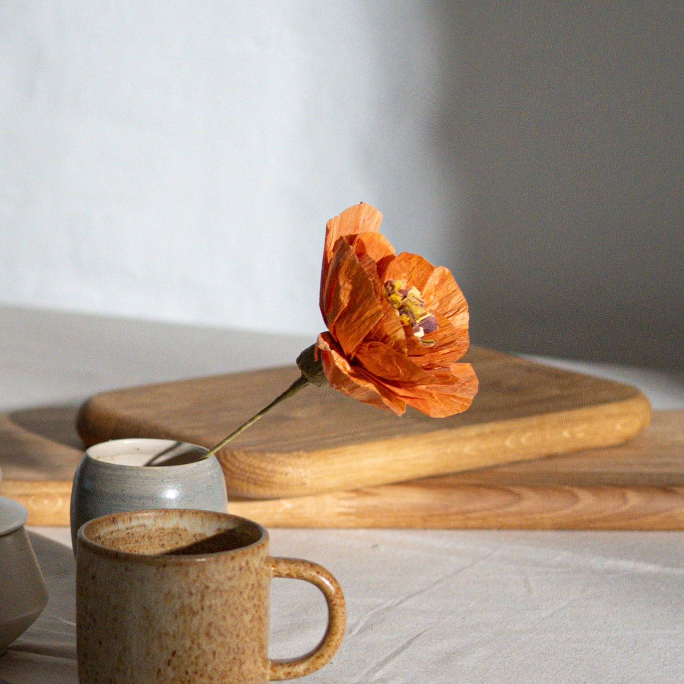 Billede af krus, vase med orange blomst og 2 tapasbræt i baggrunden